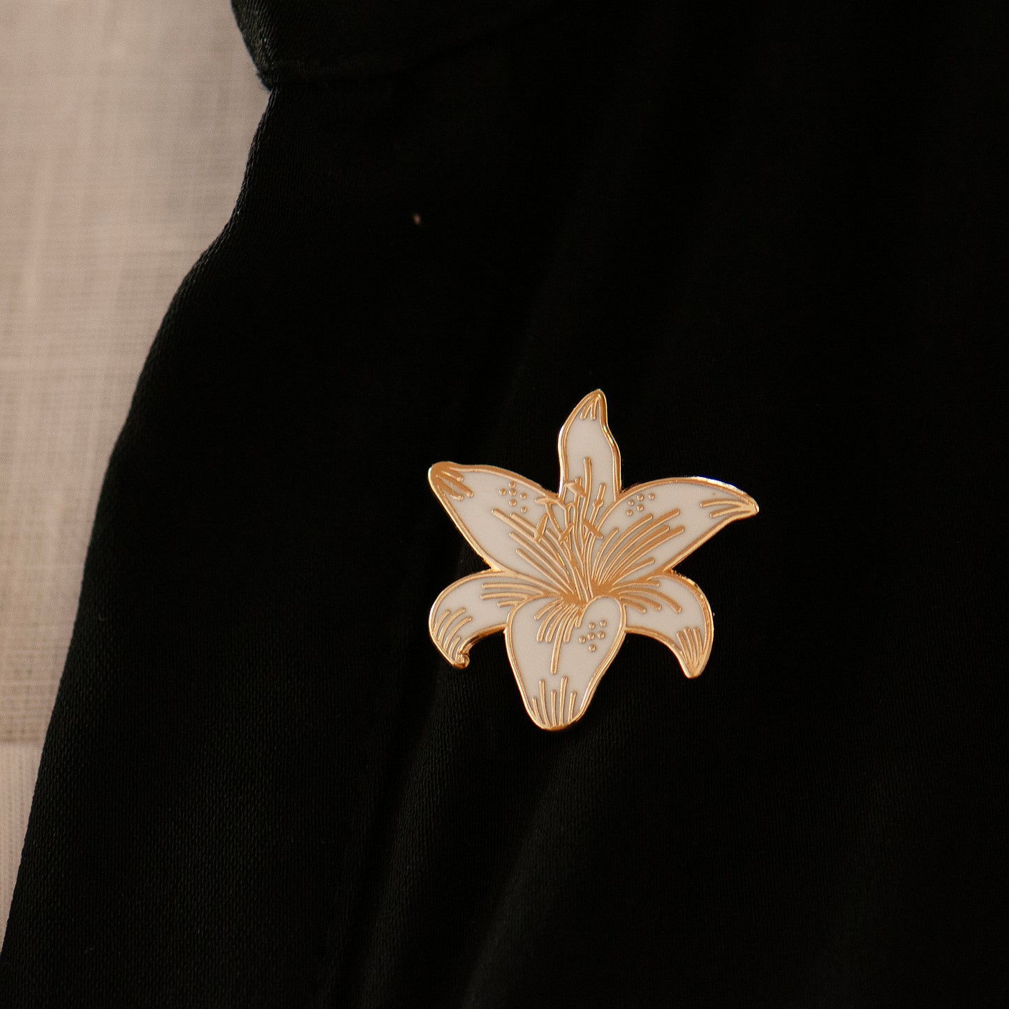 White and gold lily flower pin on lapel, showing gold detailing
