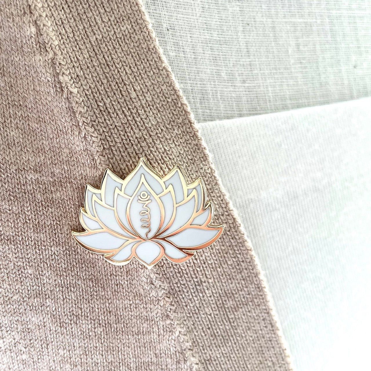 white and gold lotus flower pin on lapel, showing the unalome symbol picked out in gold detailing