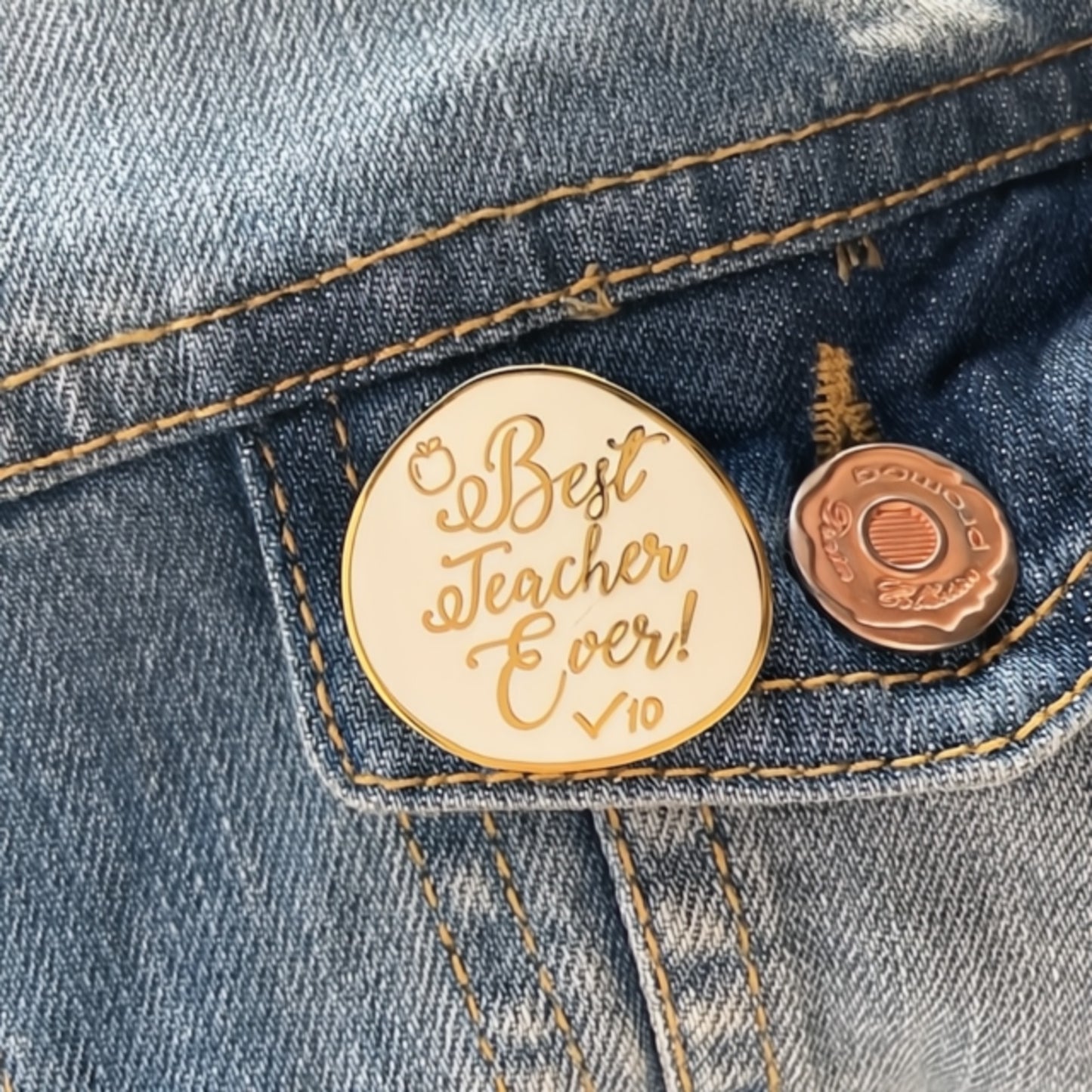 Gold and white 'Best Teacher Ever' pin on a denim jacket.