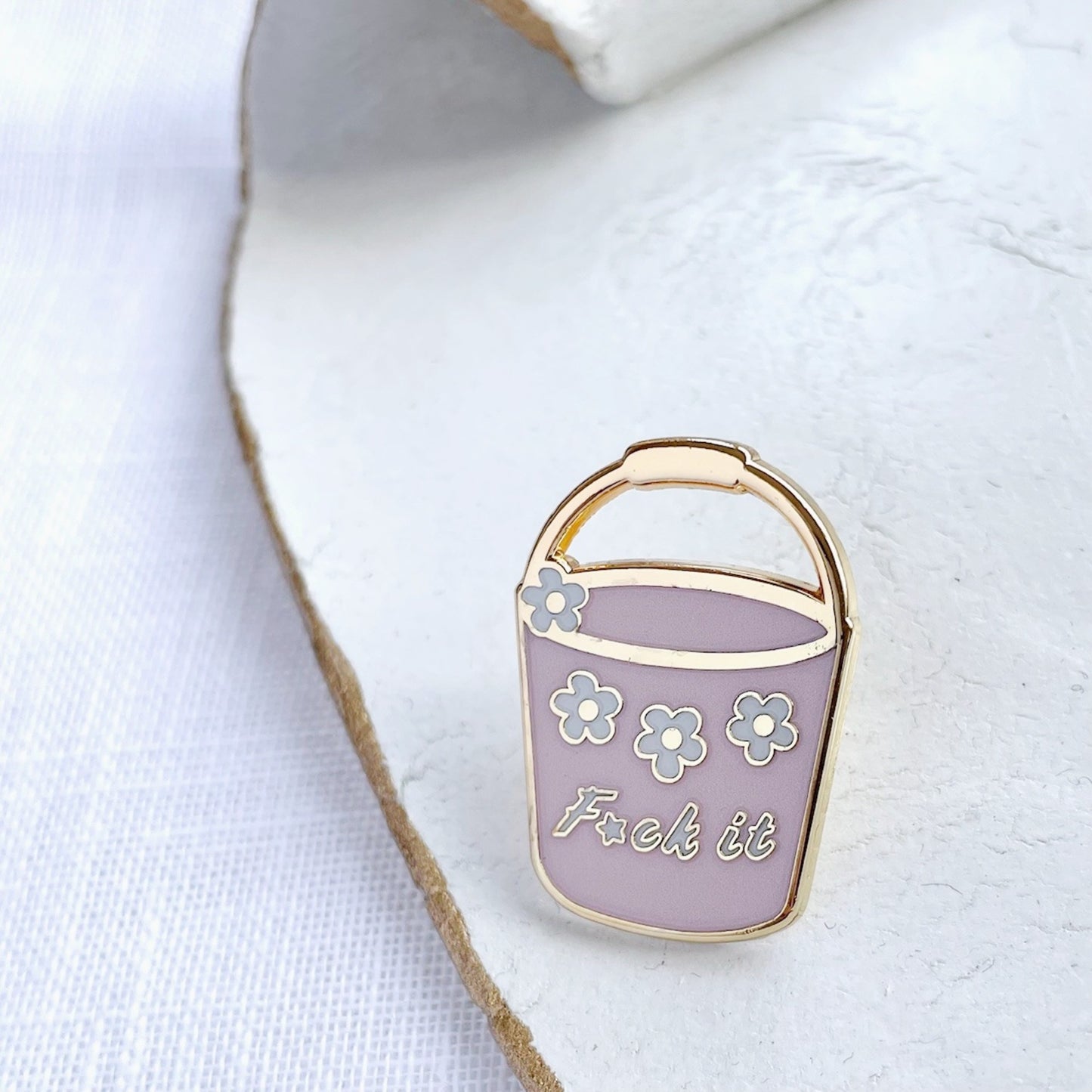 Enamel pin shaped like a pink bucket with flowers and text on a white background