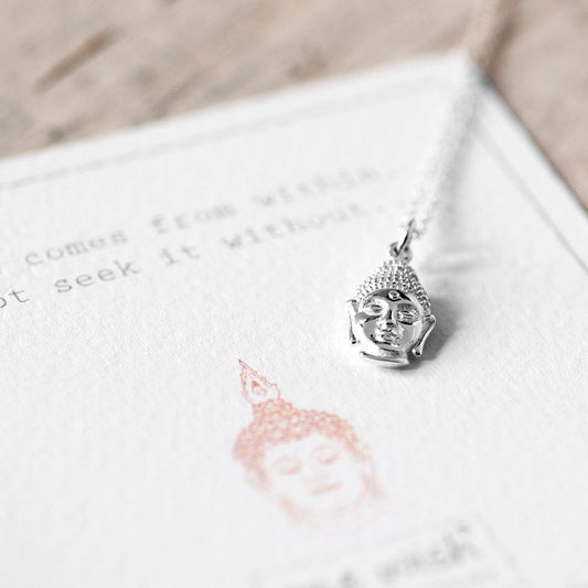 A sterling silver necklace featuring a Buddha head charm, presented on a card with a quote about peace.