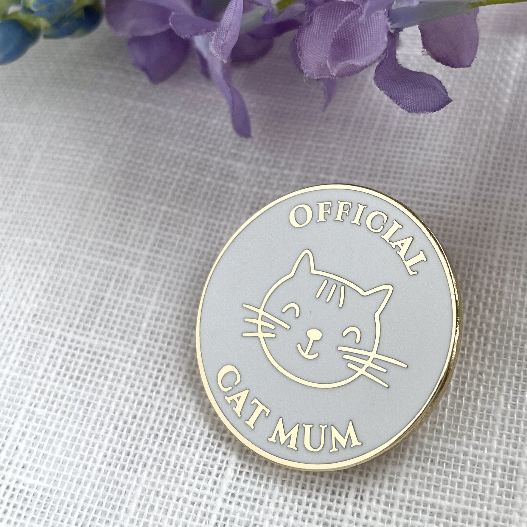 Circular badge with a cat illustration and 'Official Cat Mum' text on a textured fabric background.