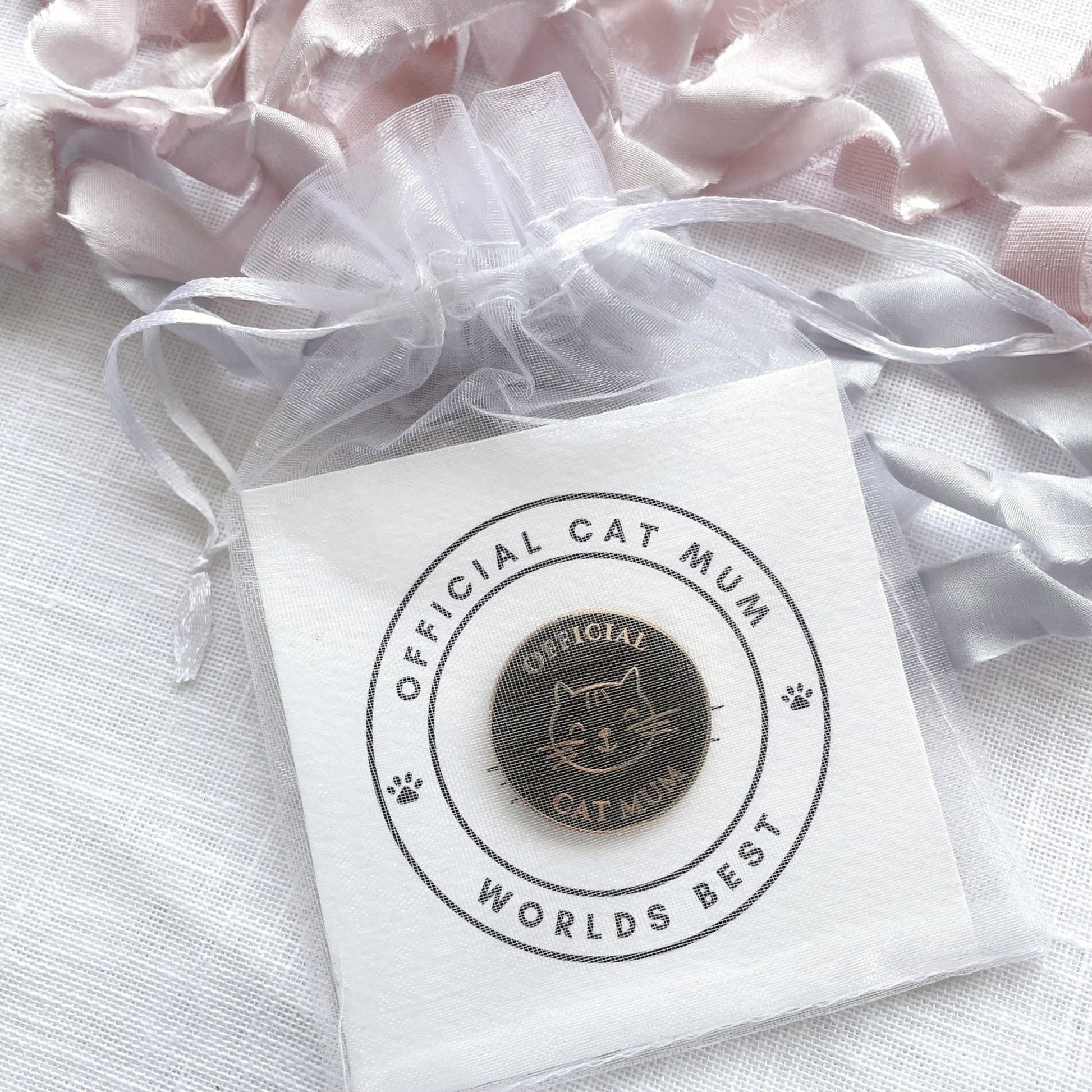 Pin with 'Official Cat Mum, Worlds Best' text on a white gift card in chiffon pouch ready for gifting.