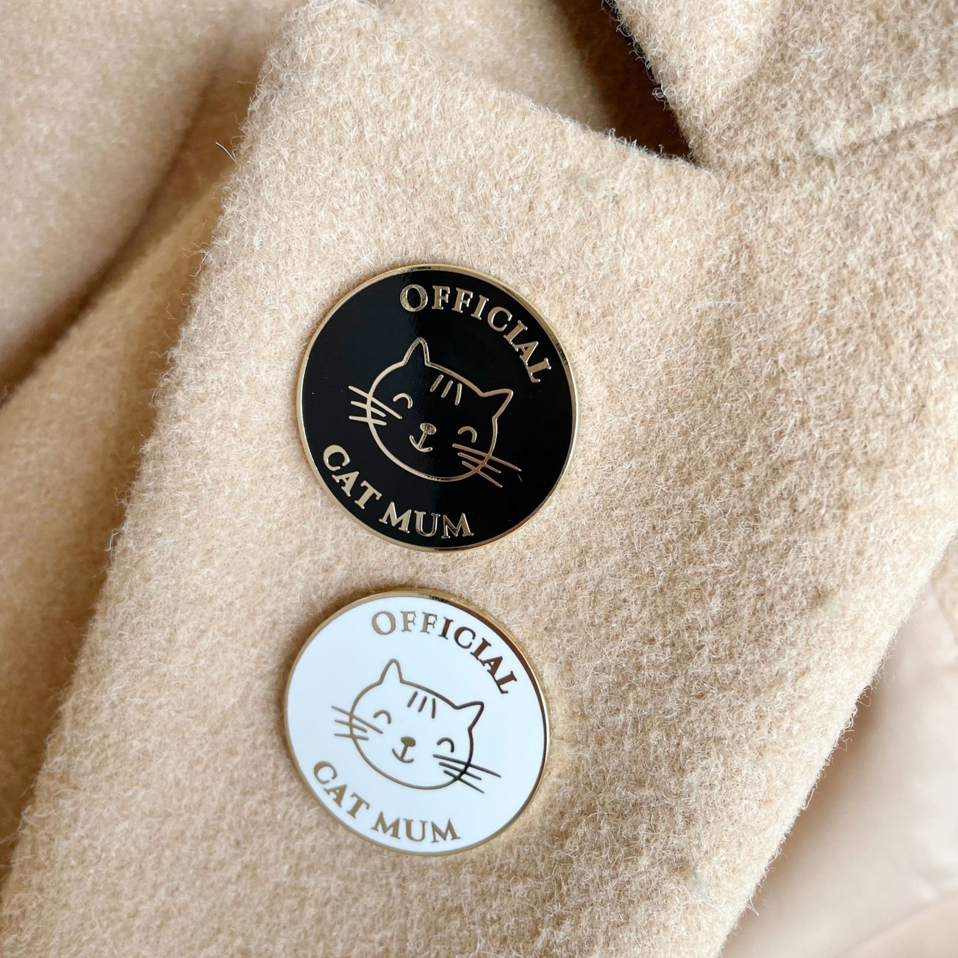 Two 'Official Cat Mum' pins on a textured beige coat lapel