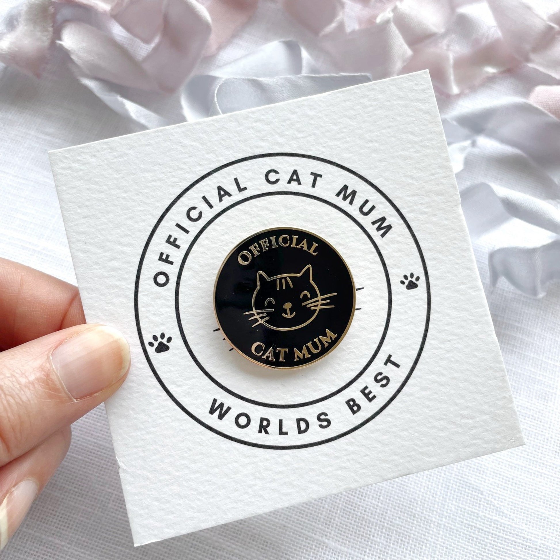 Pin with 'Official Cat Mum, Worlds Best' text on a white card held by a hand.