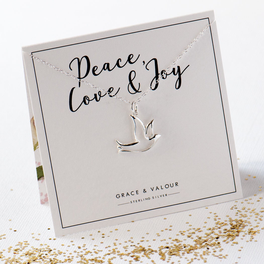 A sterling silver dove necklace in silhouette form, with the words 'PEACE AND JOY' on a gift card packaging.
