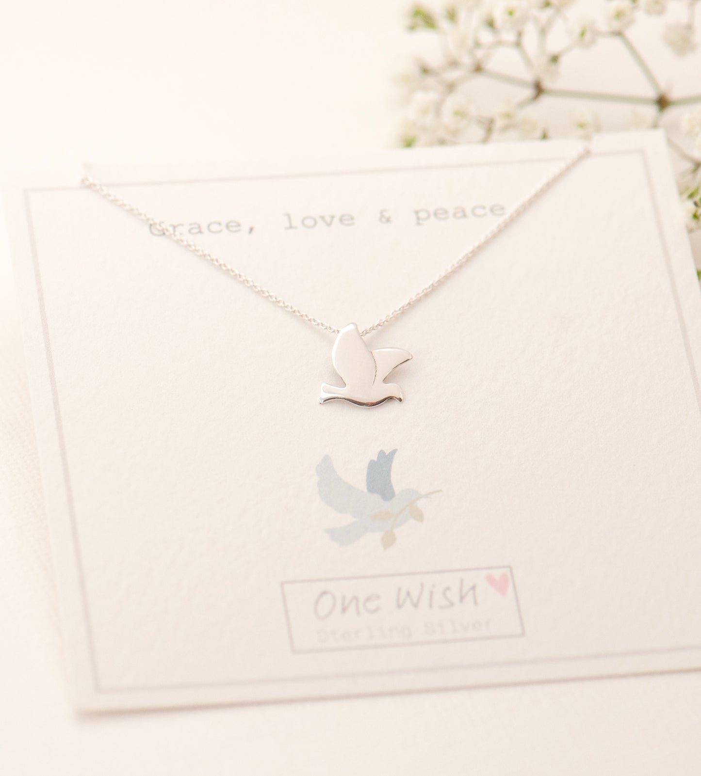 Necklace with a dove pendant on a white gift card with text that reads 'Grace, love and peace'