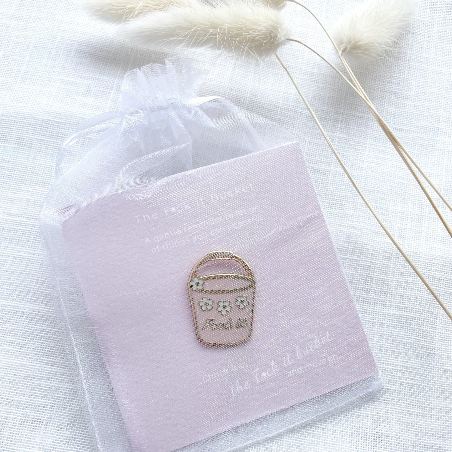 Enamel pin on a pink card with text, placed on a white fabric background