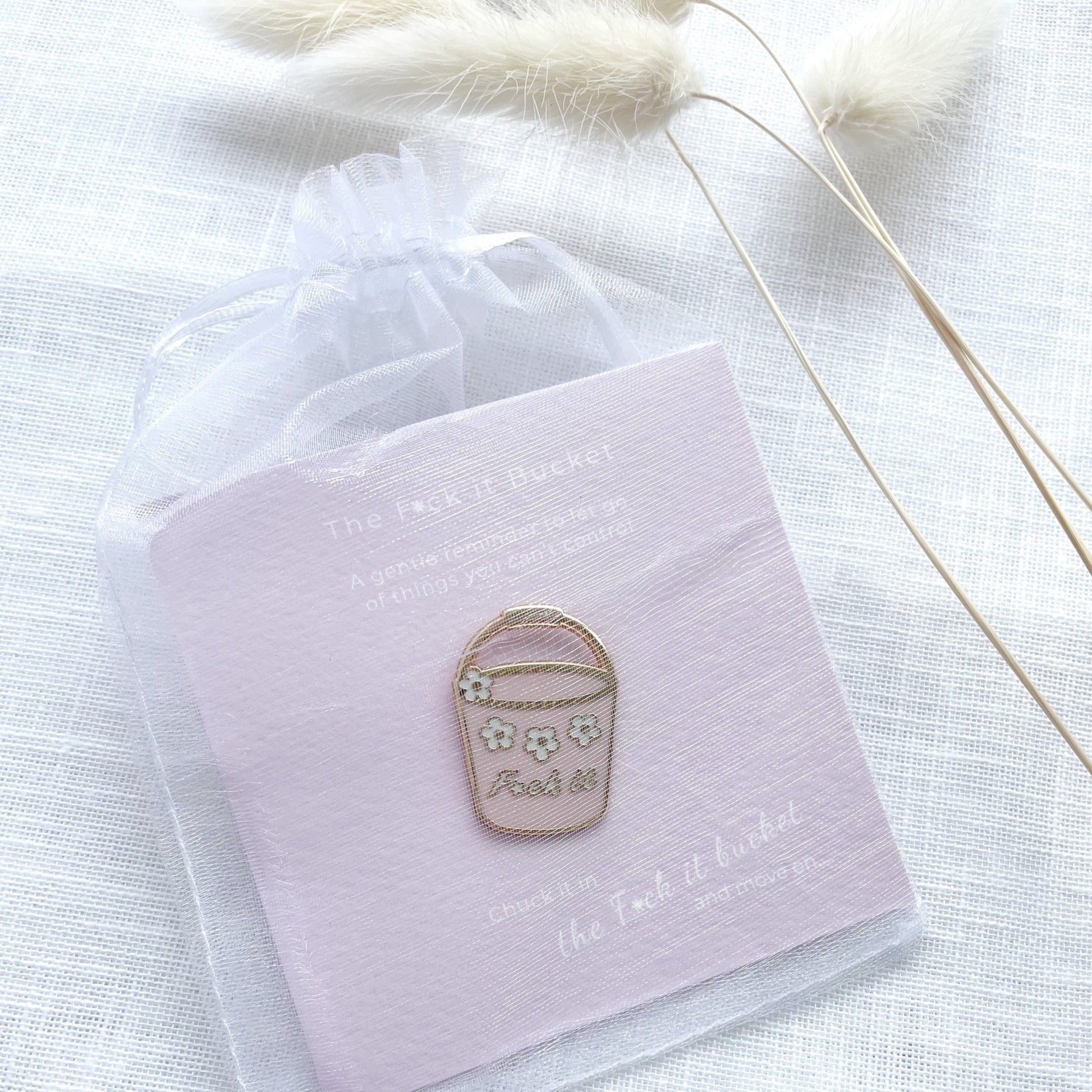 Enamel pin on a pink card with text, placed on a white fabric background