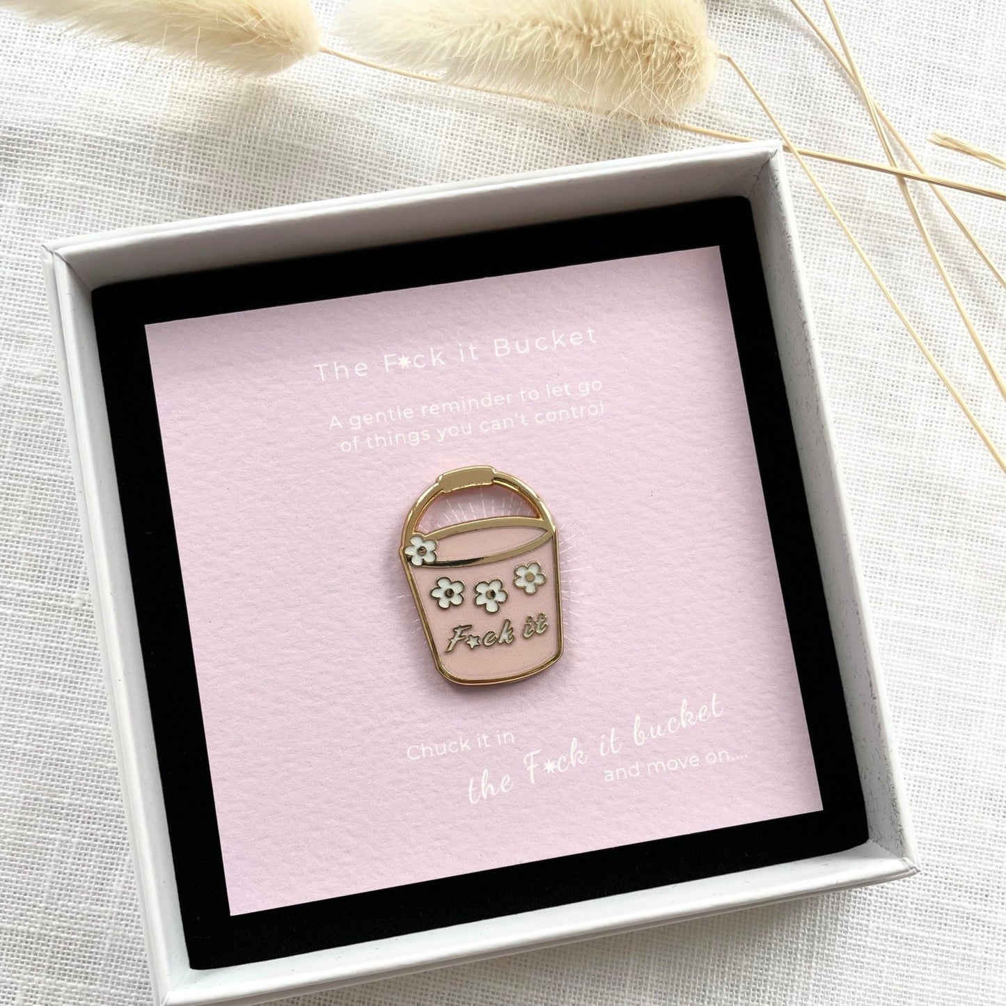 Enamel pin of a bucket with flowers in a box on a light background