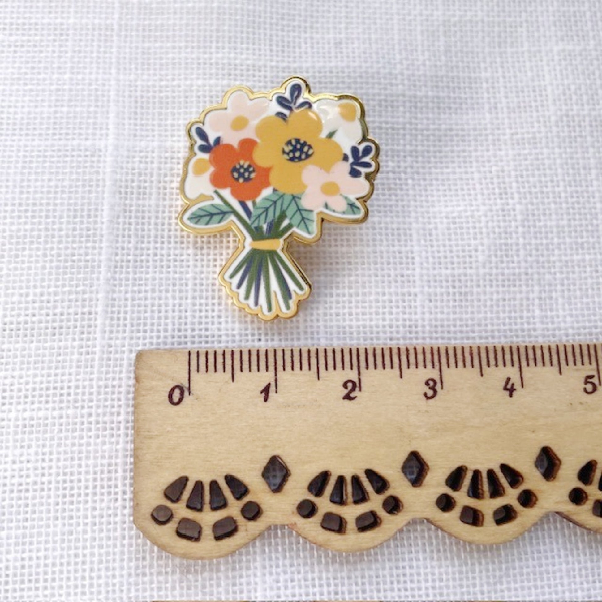 Floral pin on a white fabric background with a wooden ruler for scale.