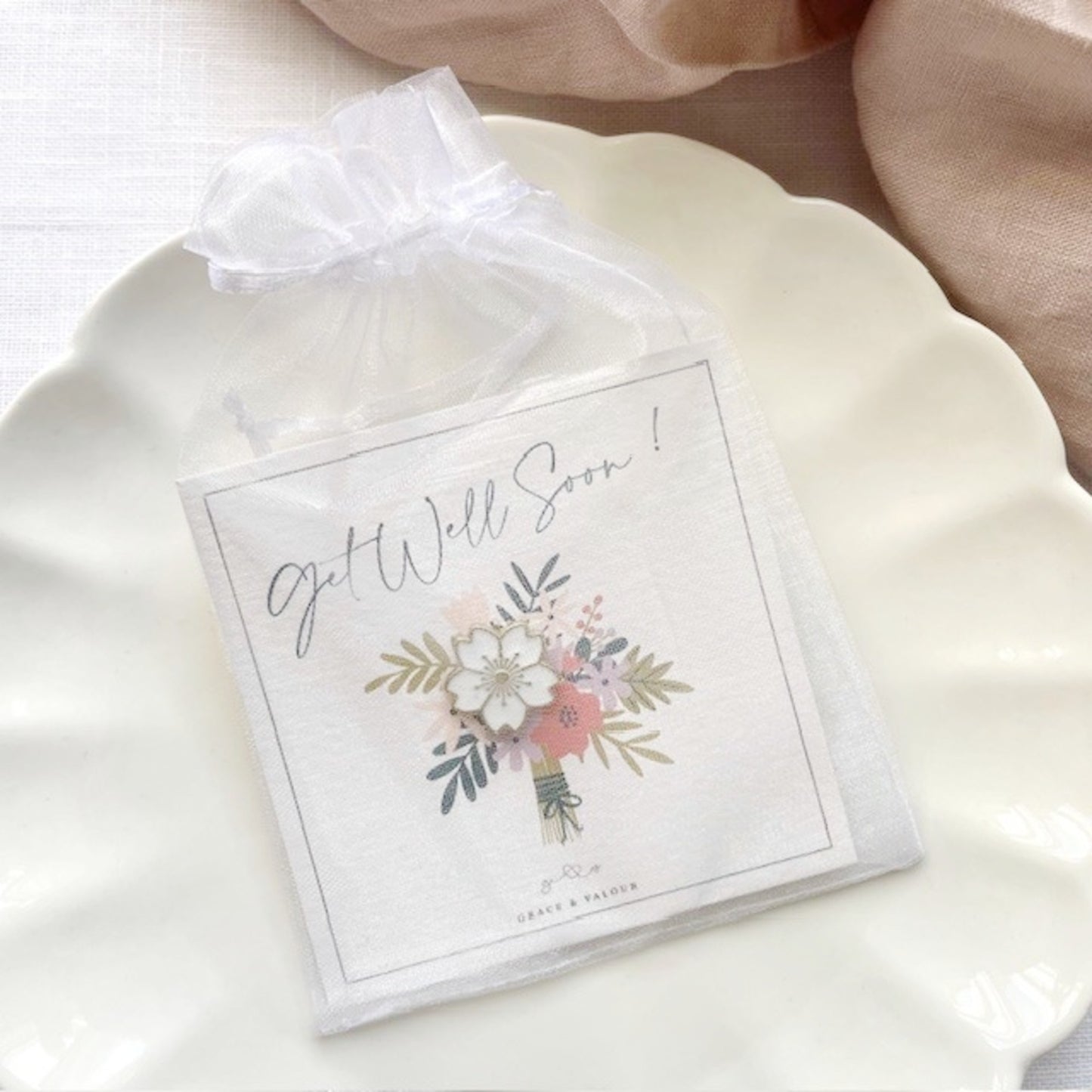 Get well soon gift card with a white enamel flower pin among the flowers in a chiffon pouch ready for gifting.