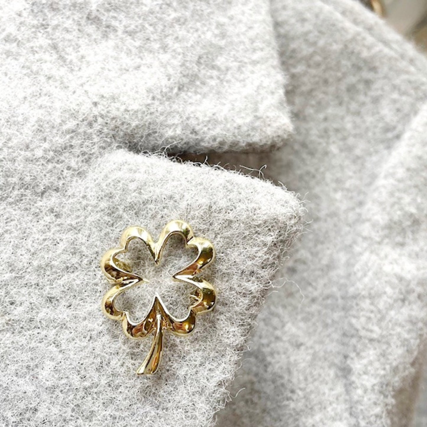 Gold four-leaf clover brooch on a textured gray jacket lapel
