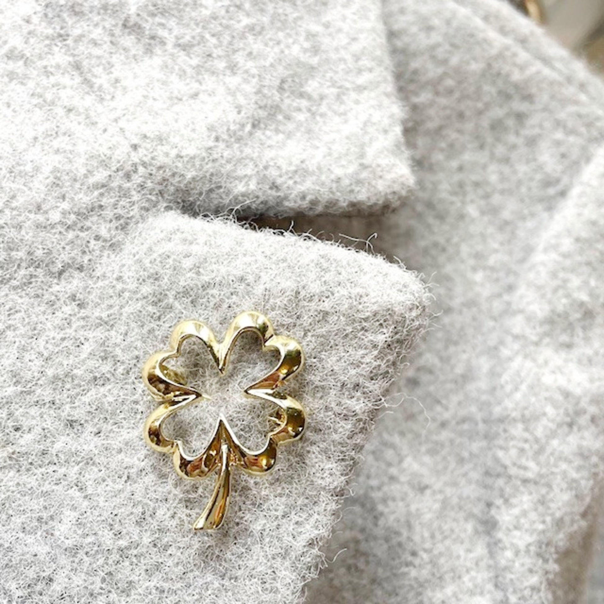 Gold four-leaf clover brooch on a textured gray jacket lapel