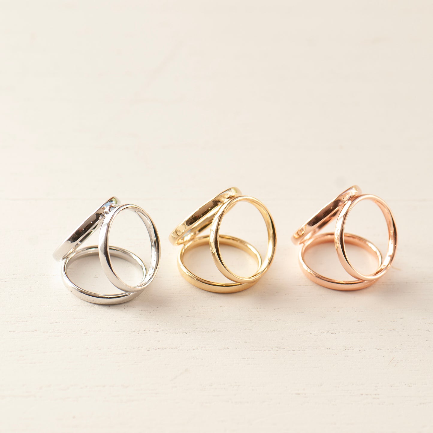 Three scarf rings in silver, gold, and rose gold on a light beige background