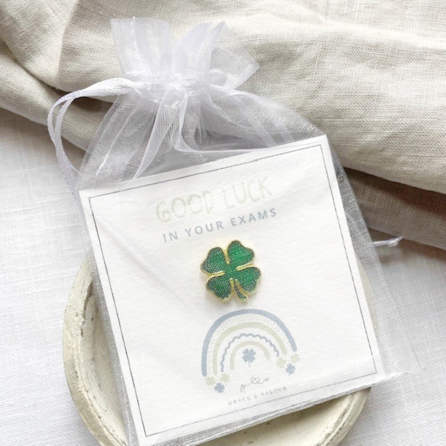 Four-leaf clover pin on a card with 'Good luck in your exams' text, wrapped in a sweet chiffon pouch ready for gifting.