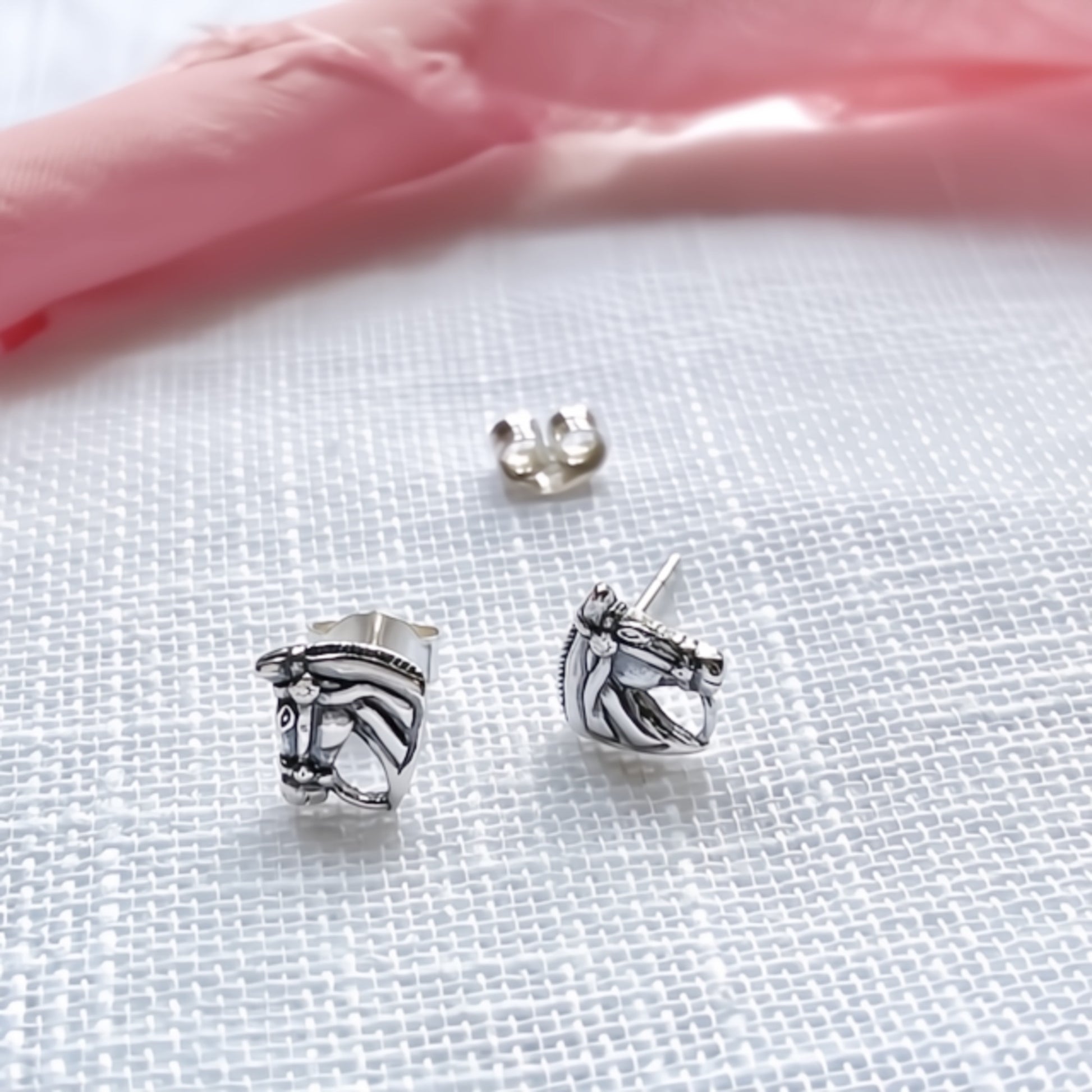 Silver horse head earrings on a white fabric background