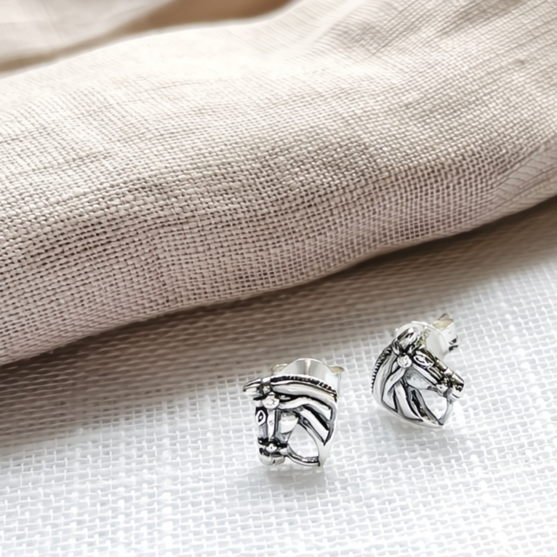 Silver horse head earrings on a textured fabric background