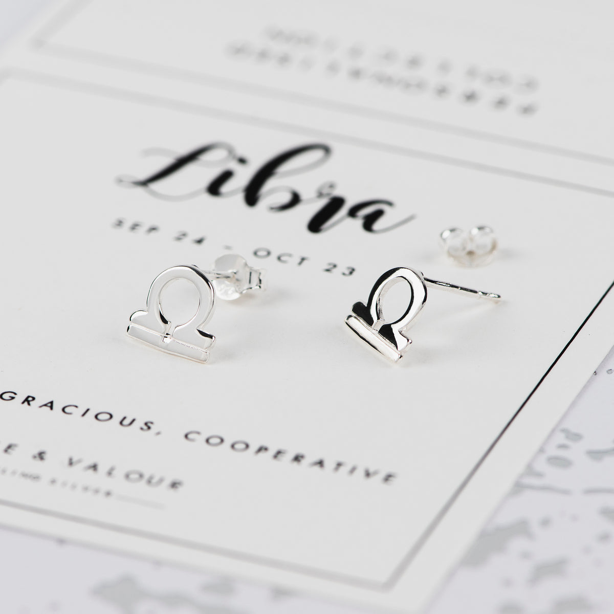 Sterling silver Libra zodiac sign stud earrings displayed on a white Libra-themed card.