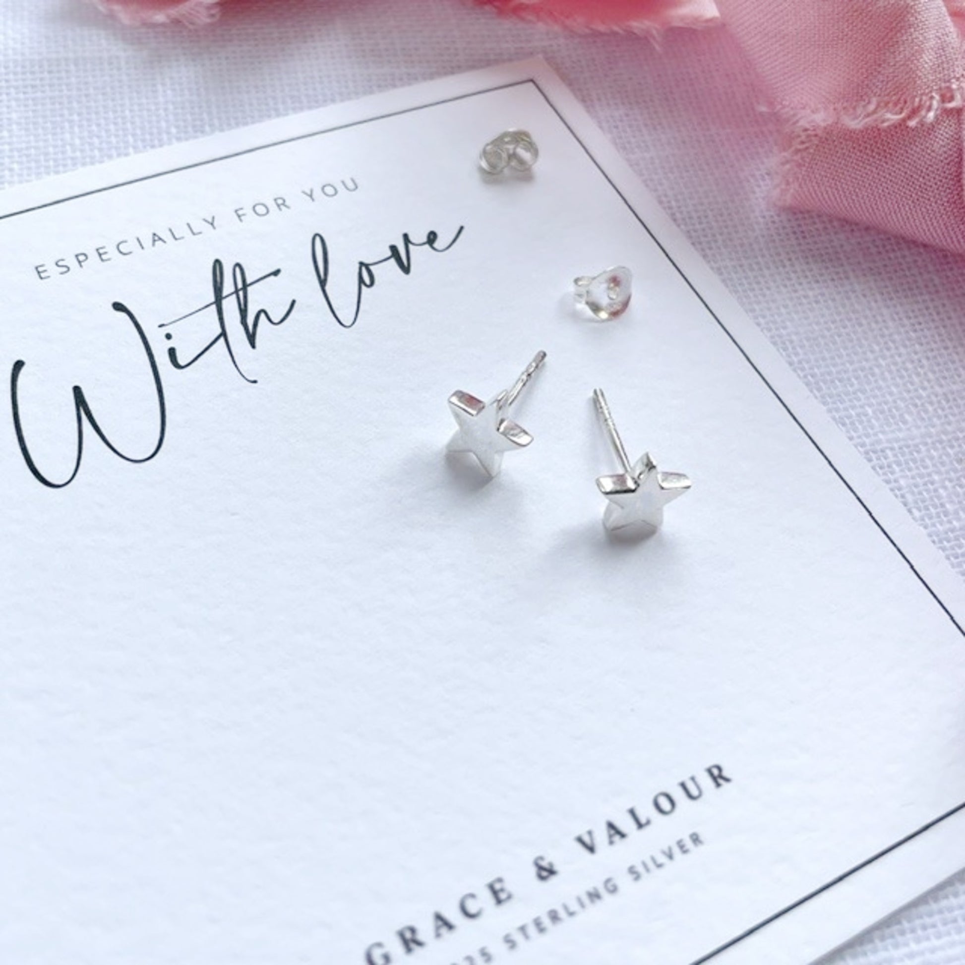 Sterling silver star-shaped stud earrings displayed on a white branded card that reads 'With love' and 'Grace & Valour'.