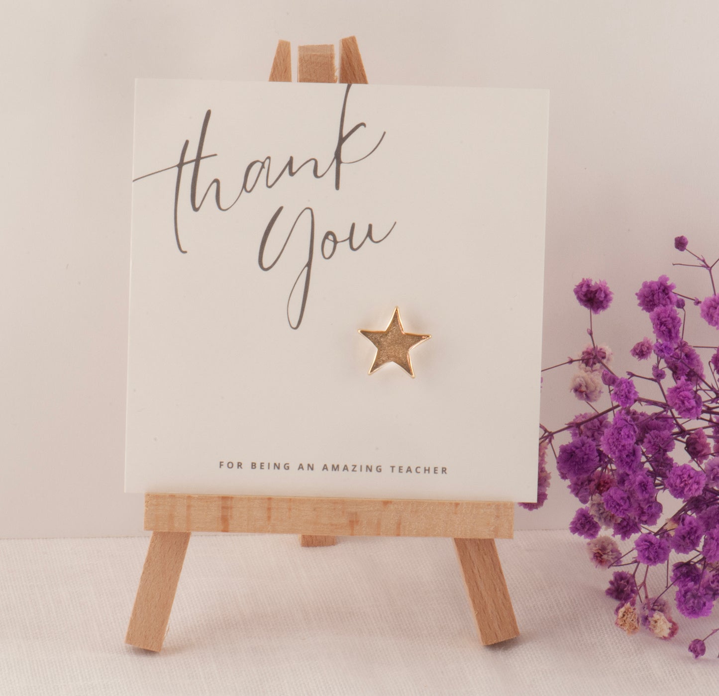 Card with 'Thank You for being an amazing teacher' text on a wooden easel with purple flowers.