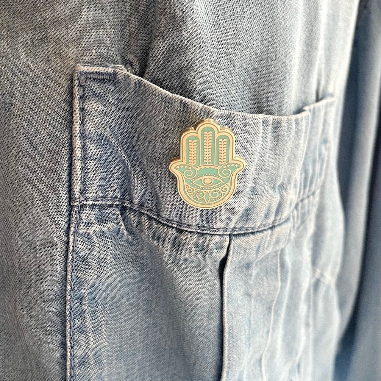 hamsa pin mint green and gold on a shirt pocket