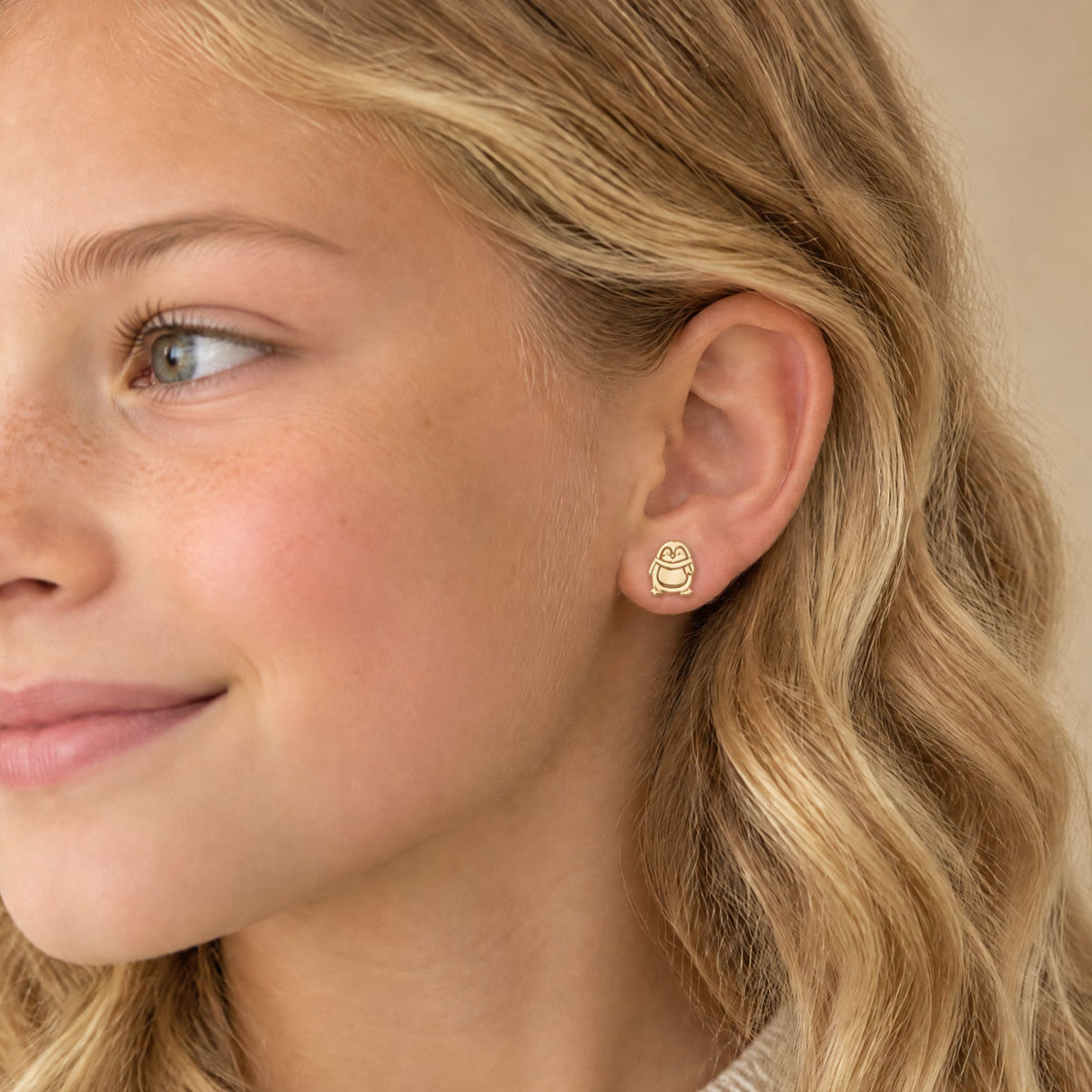 young blonde girl wearing a penguin stud earring in her left ear