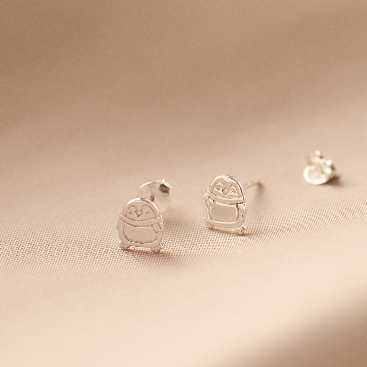 close up of a pair of penguin stud earrings on a soft fabric background
