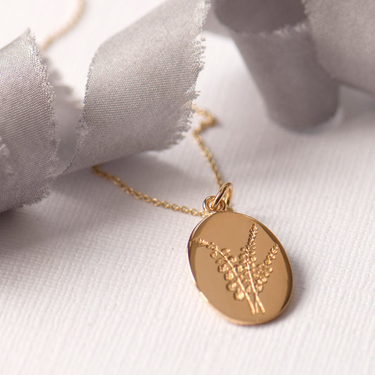 An oval-shaped gold-plated pendant featuring an engraved heather flower design, attached to a gold-plated chain.
