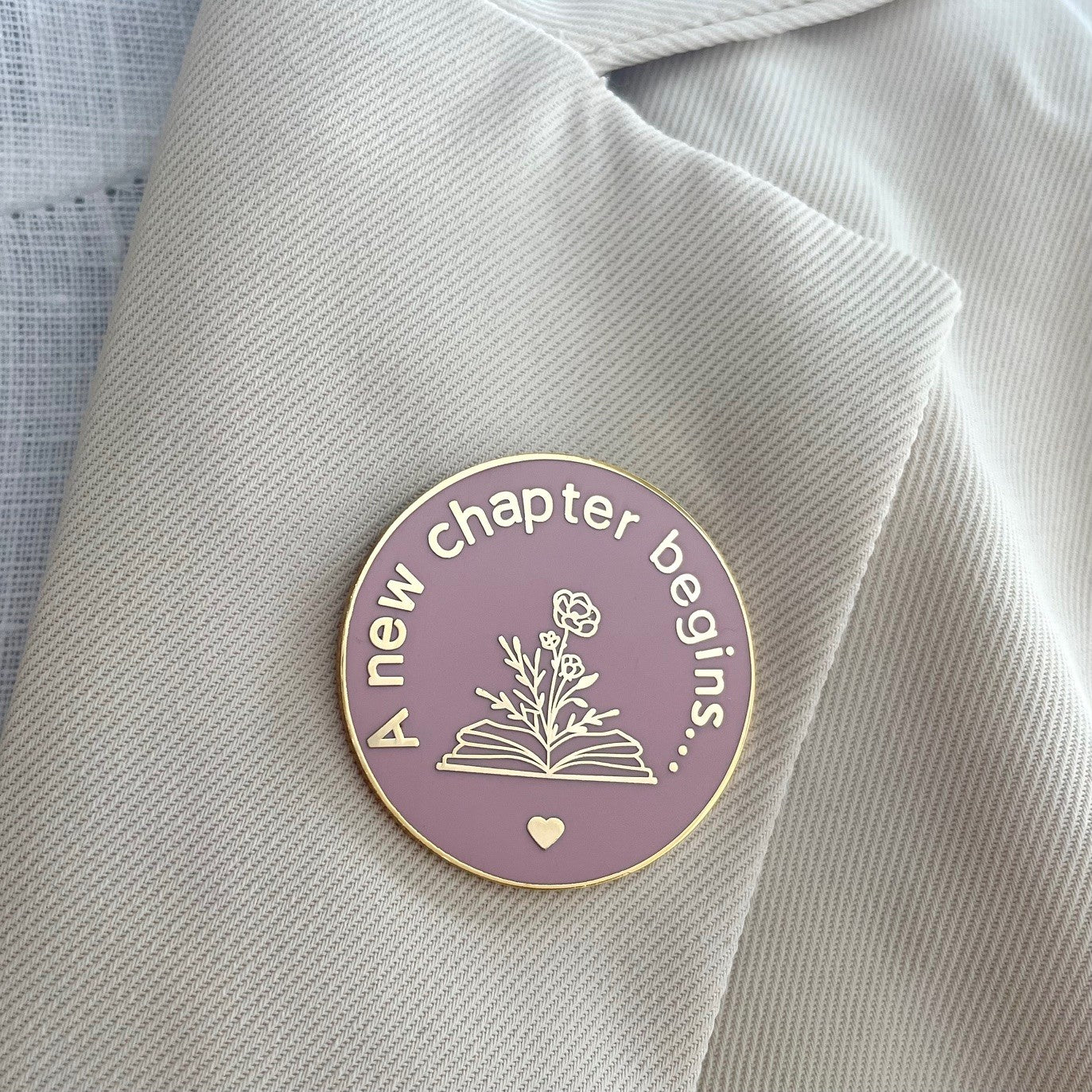 New chapter begins smoke rose and gold enamel pin on jacket lapel.