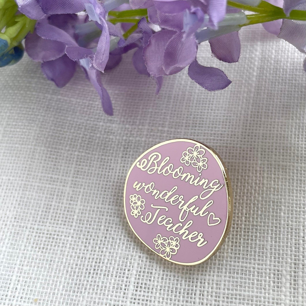Pink enamel pin with 'Blooming wonderful Teacher' text on a white fabric background