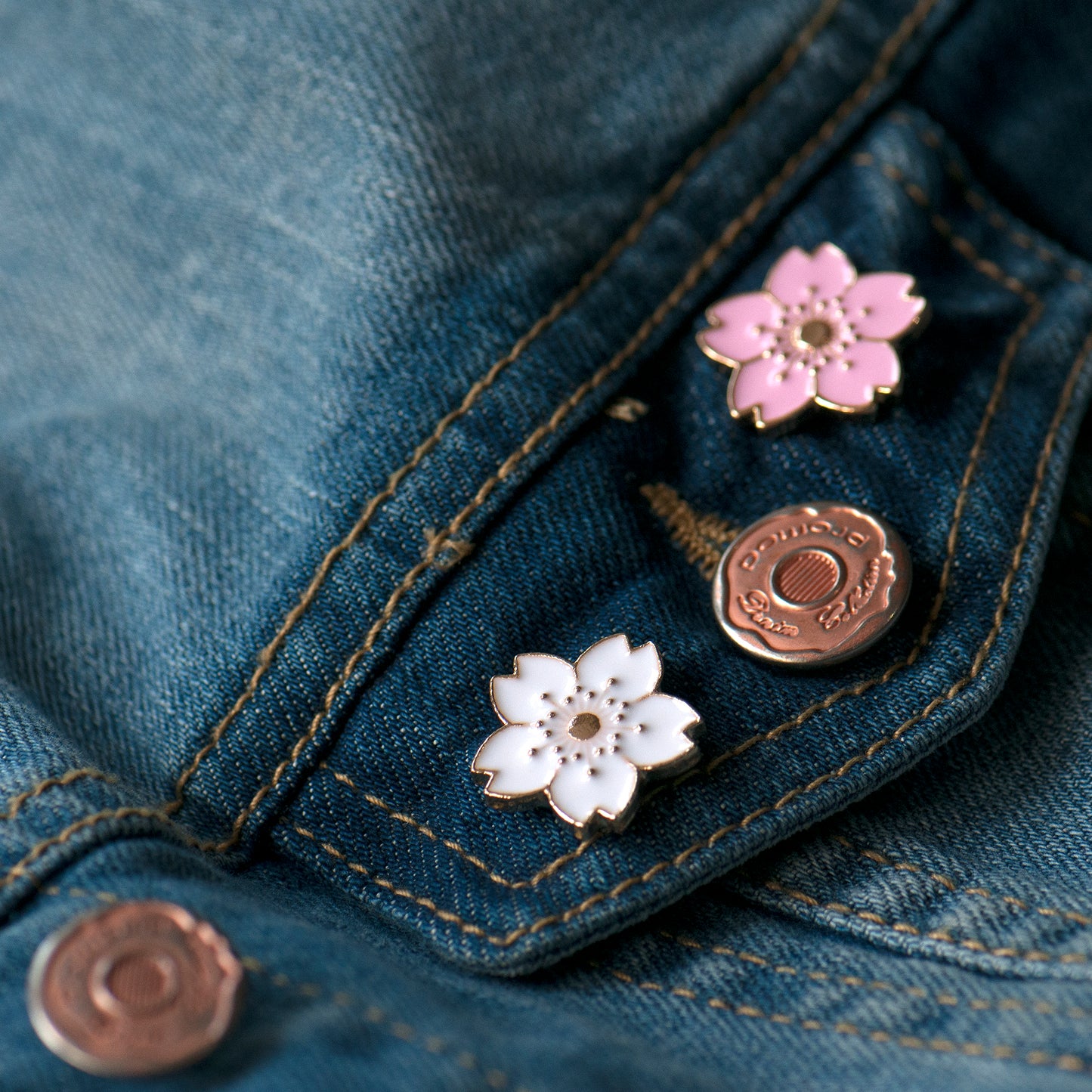 Close-up of a denim jacket with floral cherry blossom enamel pins.