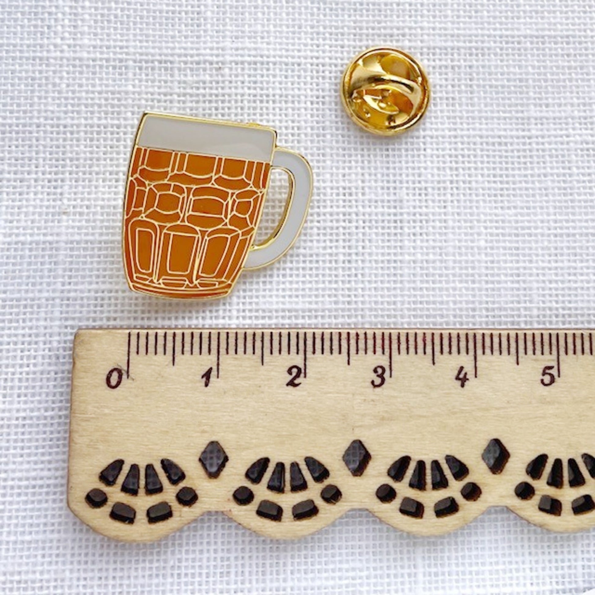 Enamel pin of a beer mug with a ruler for scale on a white background