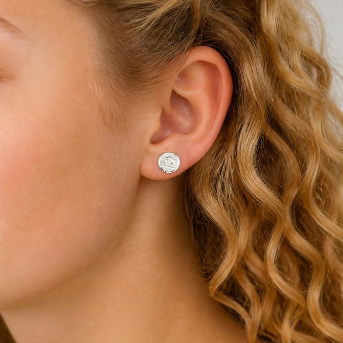 model wears a small round stud earring engraved with a zodiac sign for libra