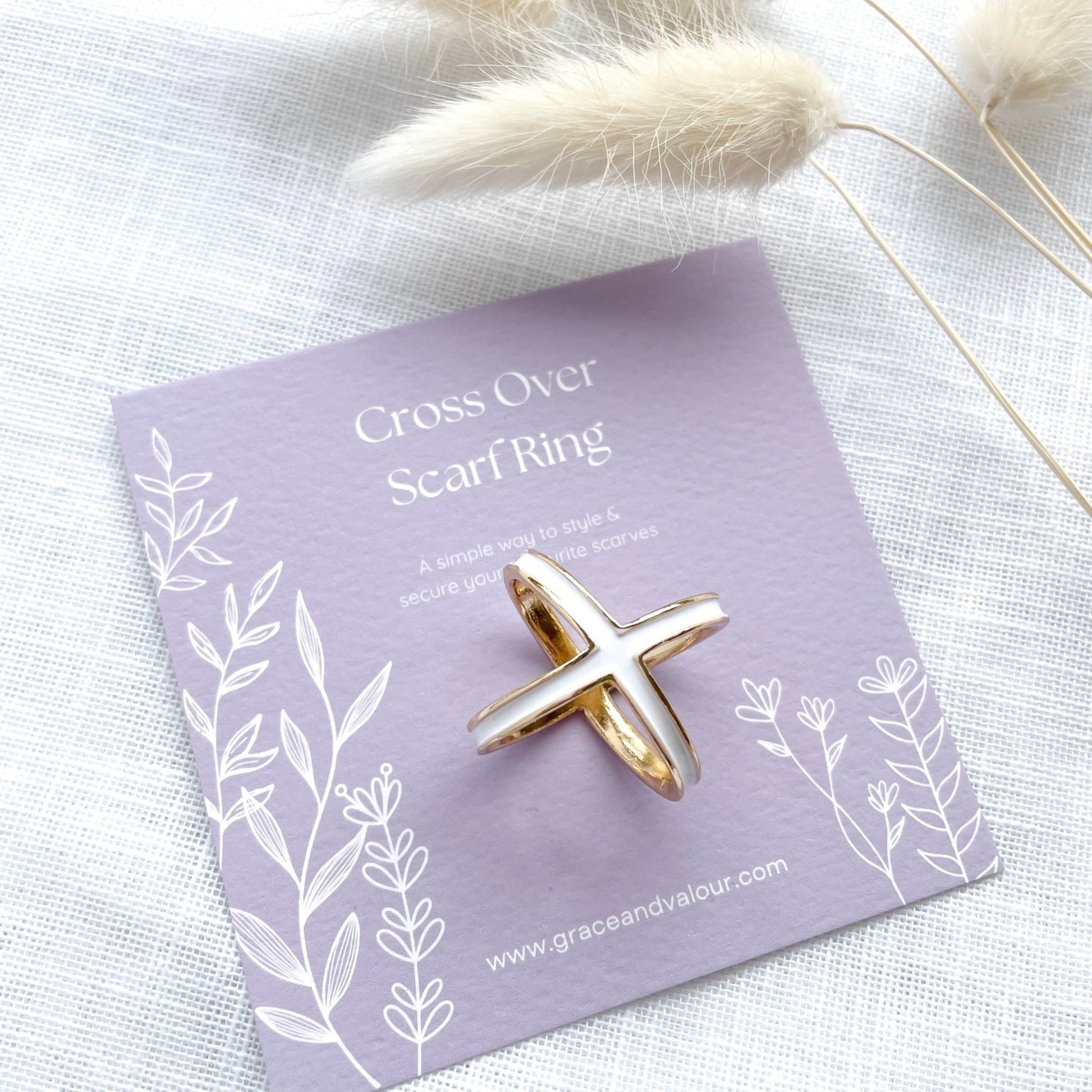 Gold scarf ring on a purple card with 'Cross Over Scarf Ring' text, placed on a light fabric background.