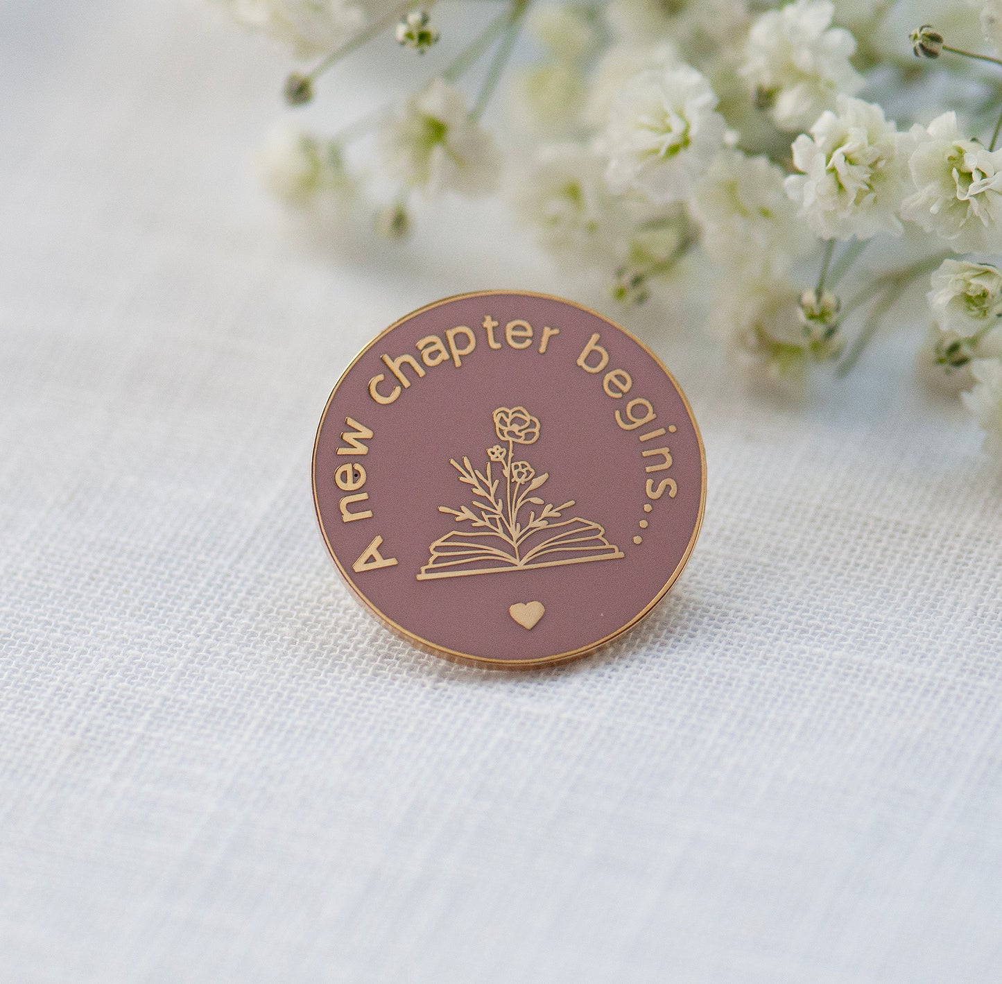 Smoke rose and gold new chapter pin, showing a book with flowers growing out of it as a new chapter