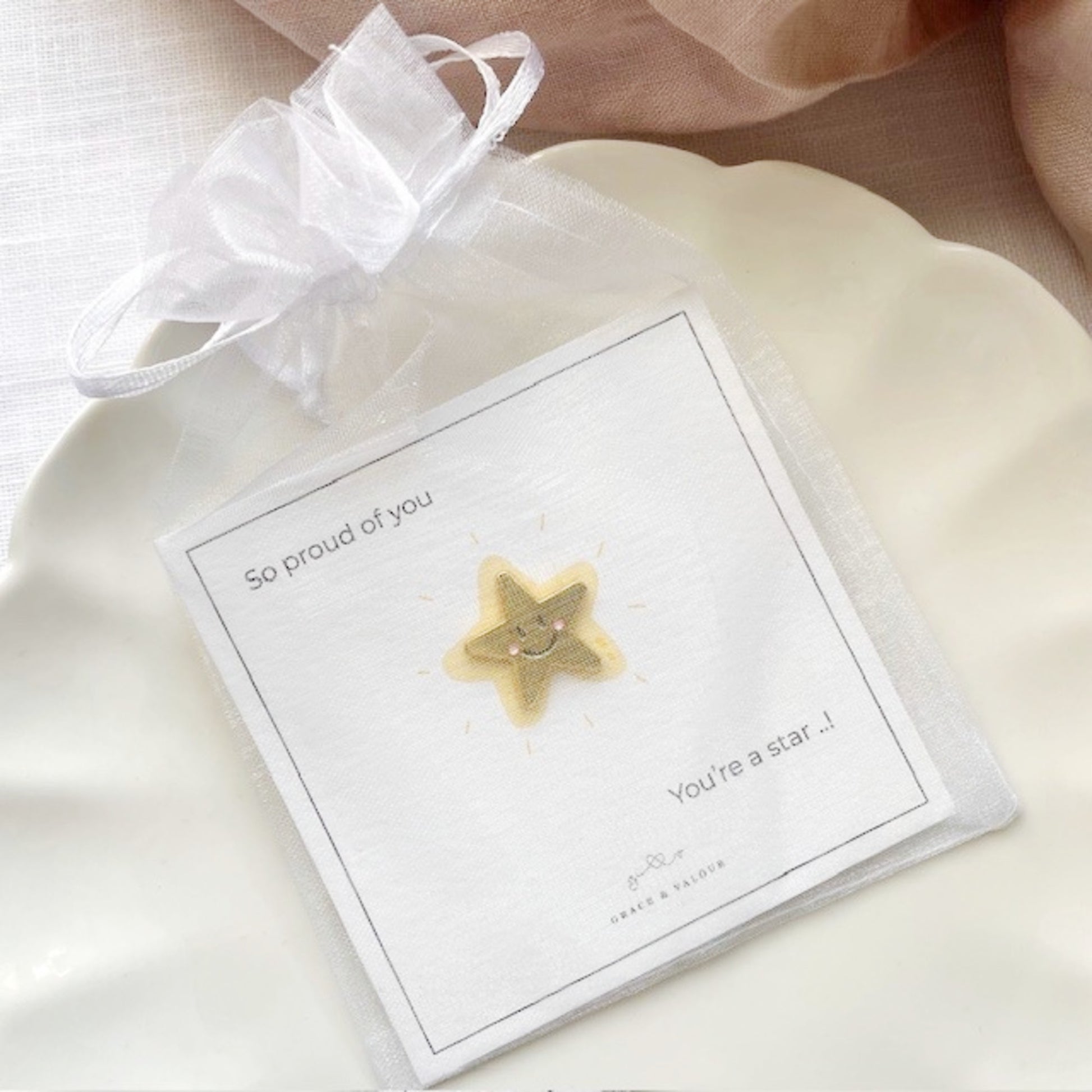 Gold star-shaped pin on a card with text, tin a chiffon pouch, ready for gifting