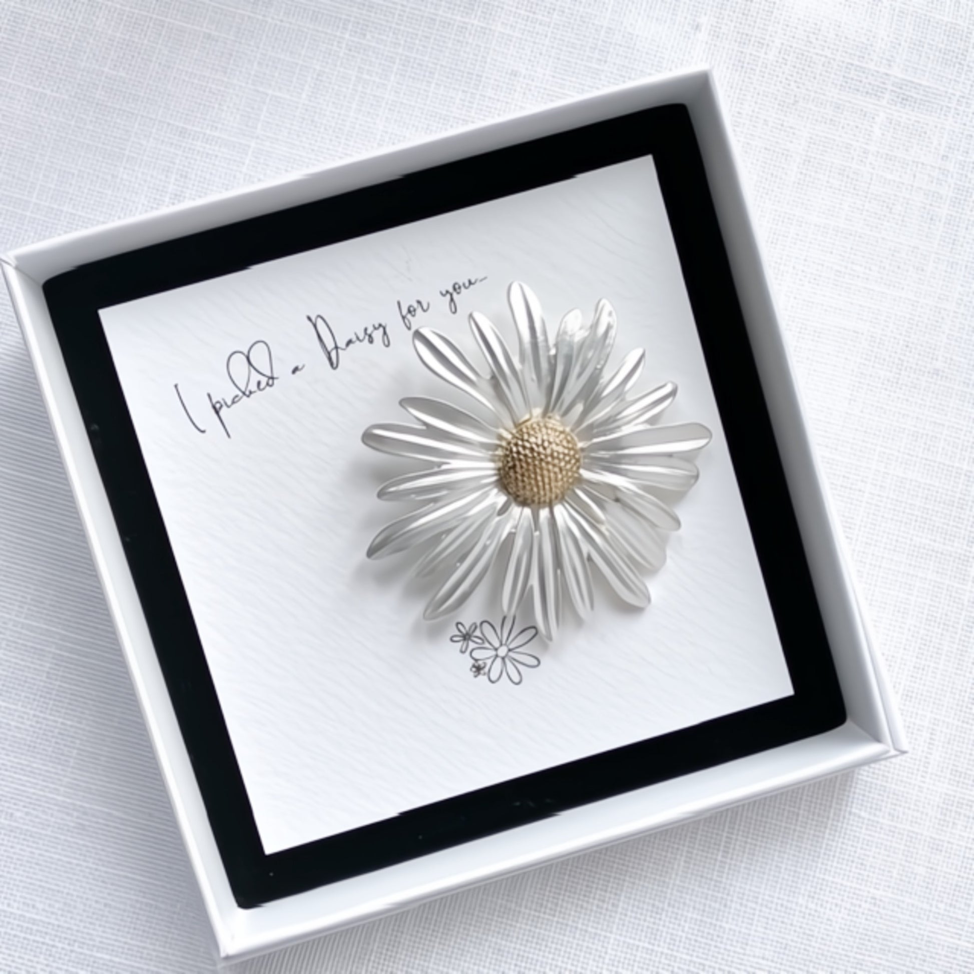 White daisy-shaped brooch in a gift box with a gift card inside