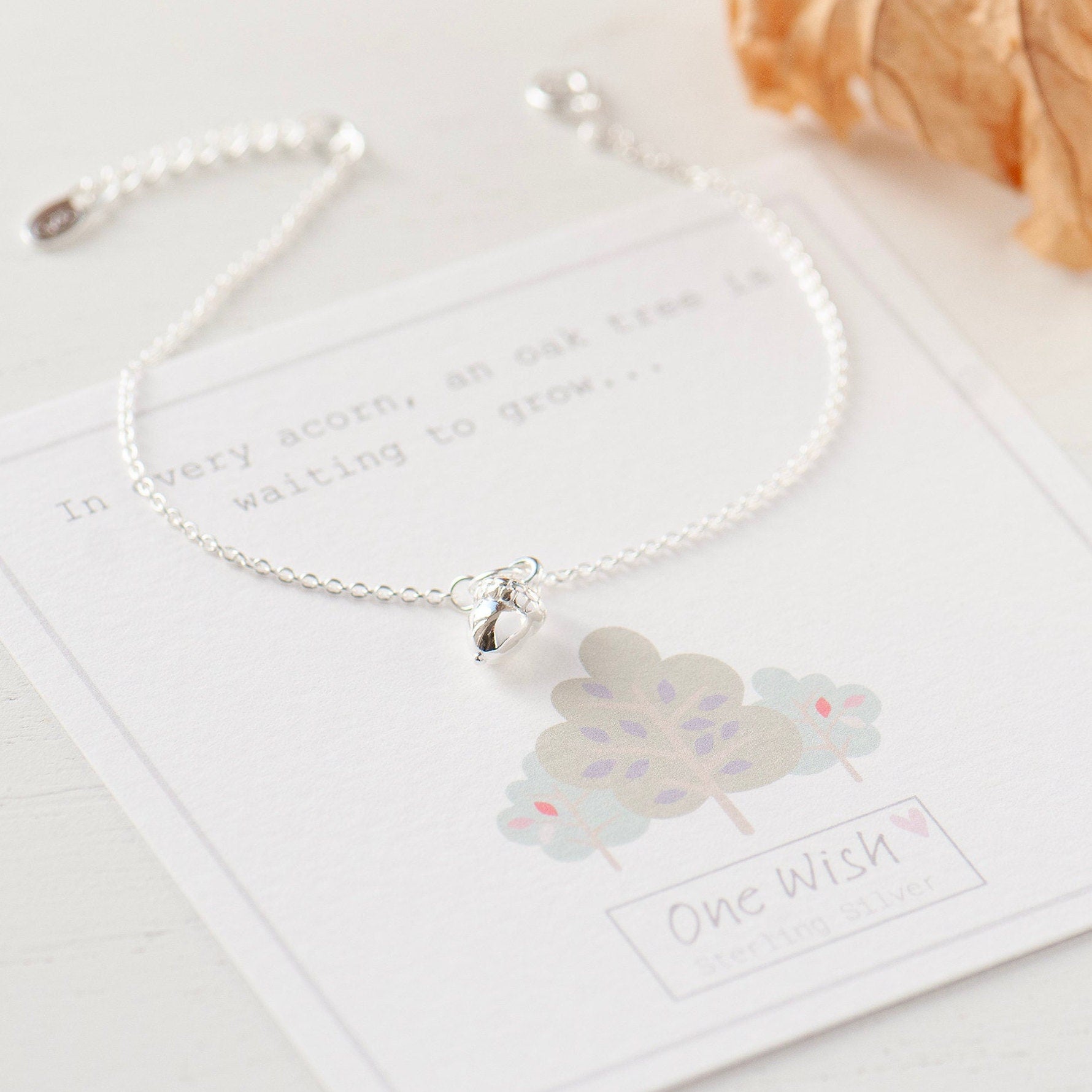A sterling silver acorn charm bracelet with a cable chain and spring ring clasp, displayed on a card with an acorn and oak tree illustration and the text 'In every acorn an oak tree is waiting to grow.