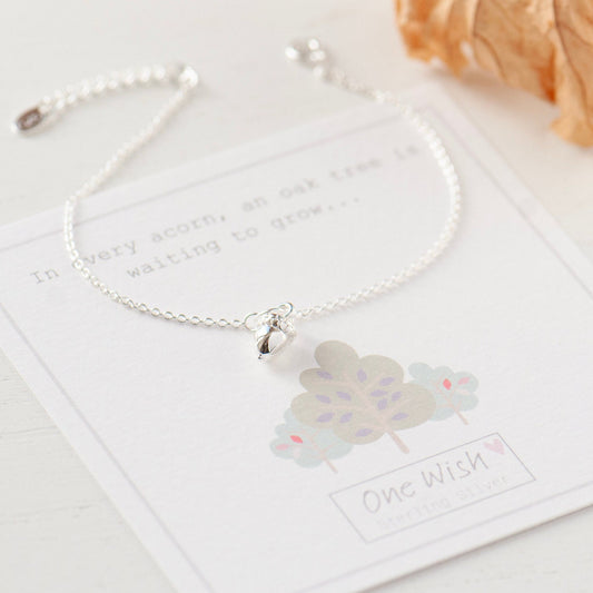 A sterling silver acorn charm bracelet with a cable chain and spring ring clasp, displayed on a card with an acorn and oak tree illustration and the text 'In every acorn an oak tree is waiting to grow.