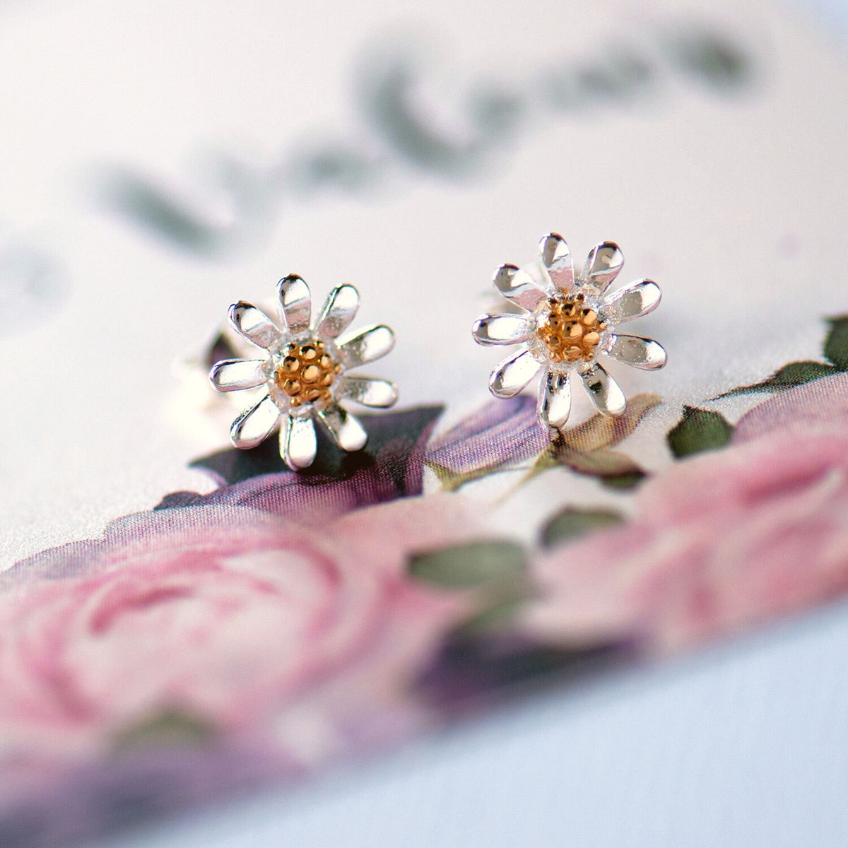 gold and silver daisy stud earrings on flower background