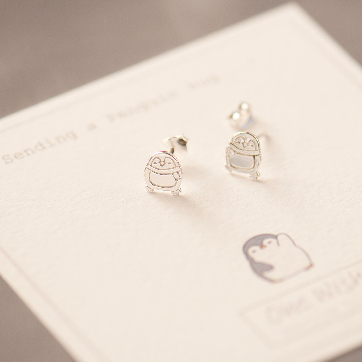 polished silver penguin flat stud earrings on a one wish gift card with a graphic of a penguin