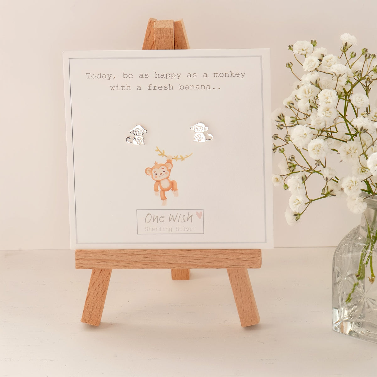 A white square card on a small wooden easel, printed with the phrase 'Today, be as happy as a monkey with a fresh banana.