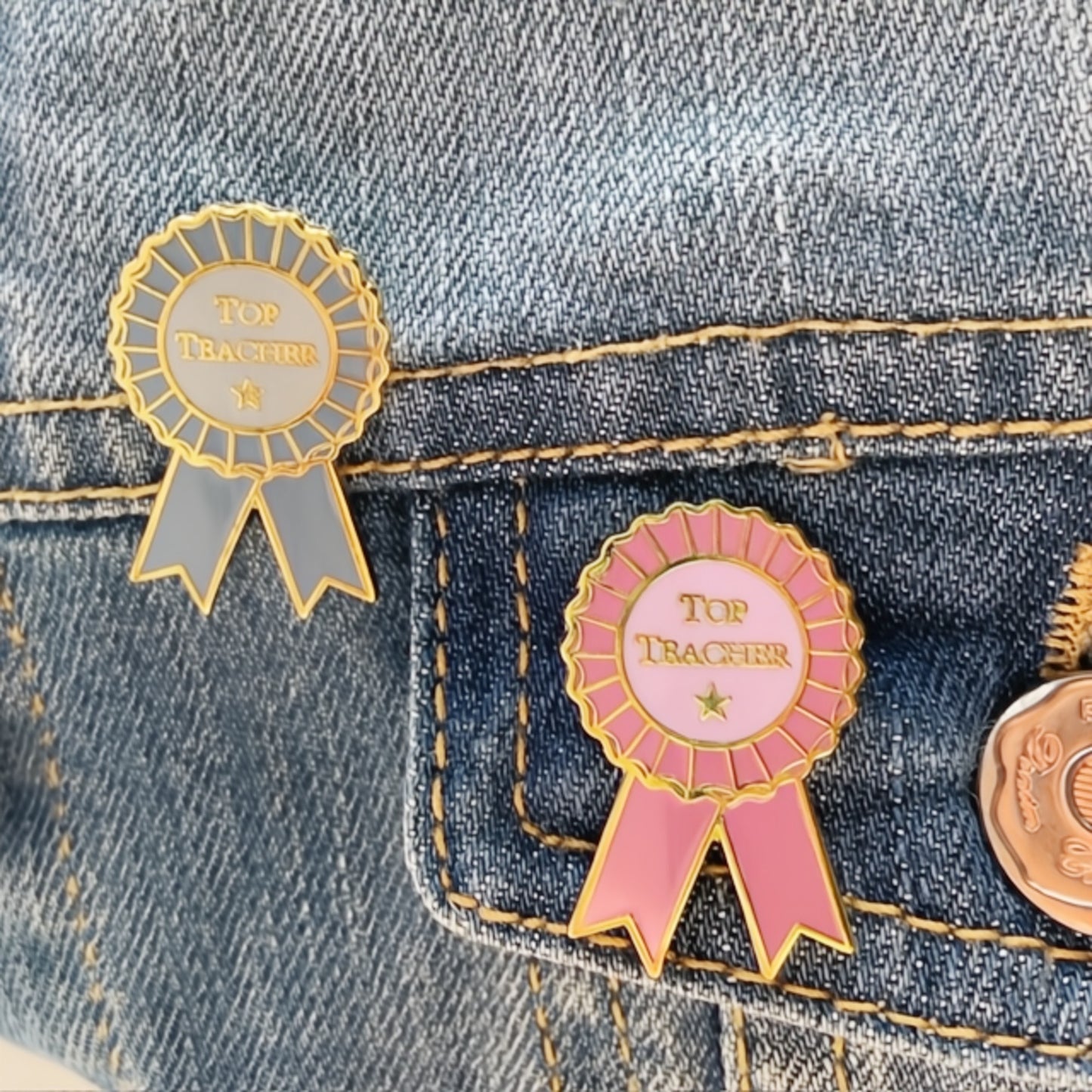 Two 'Top Teacher' pins on a denim background