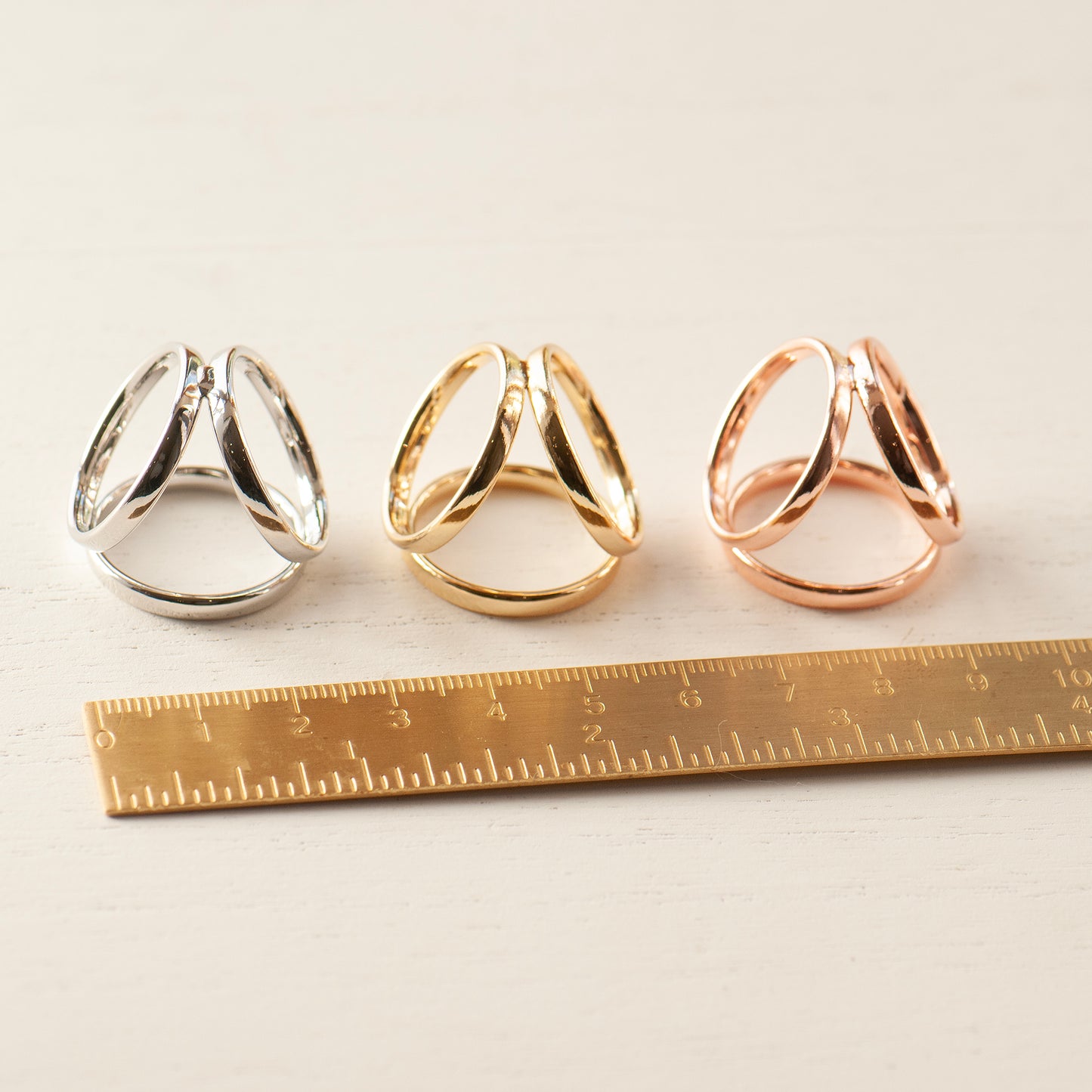 Three scarf rings in silver, gold, and rose gold next to a ruler.