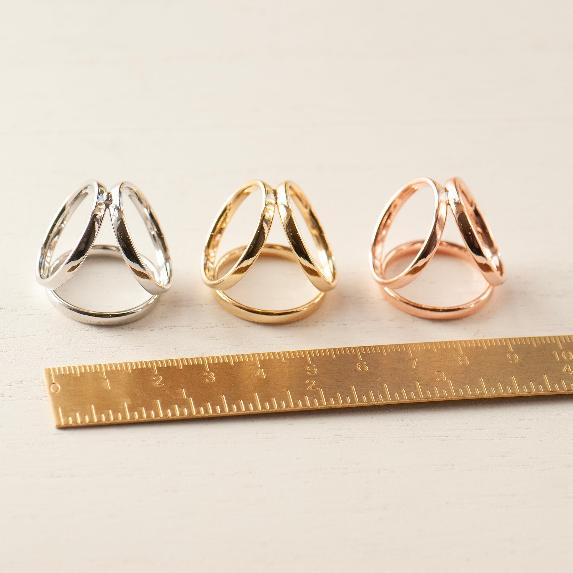 Three scarf rings in silver, gold, and rose gold next to a ruler.