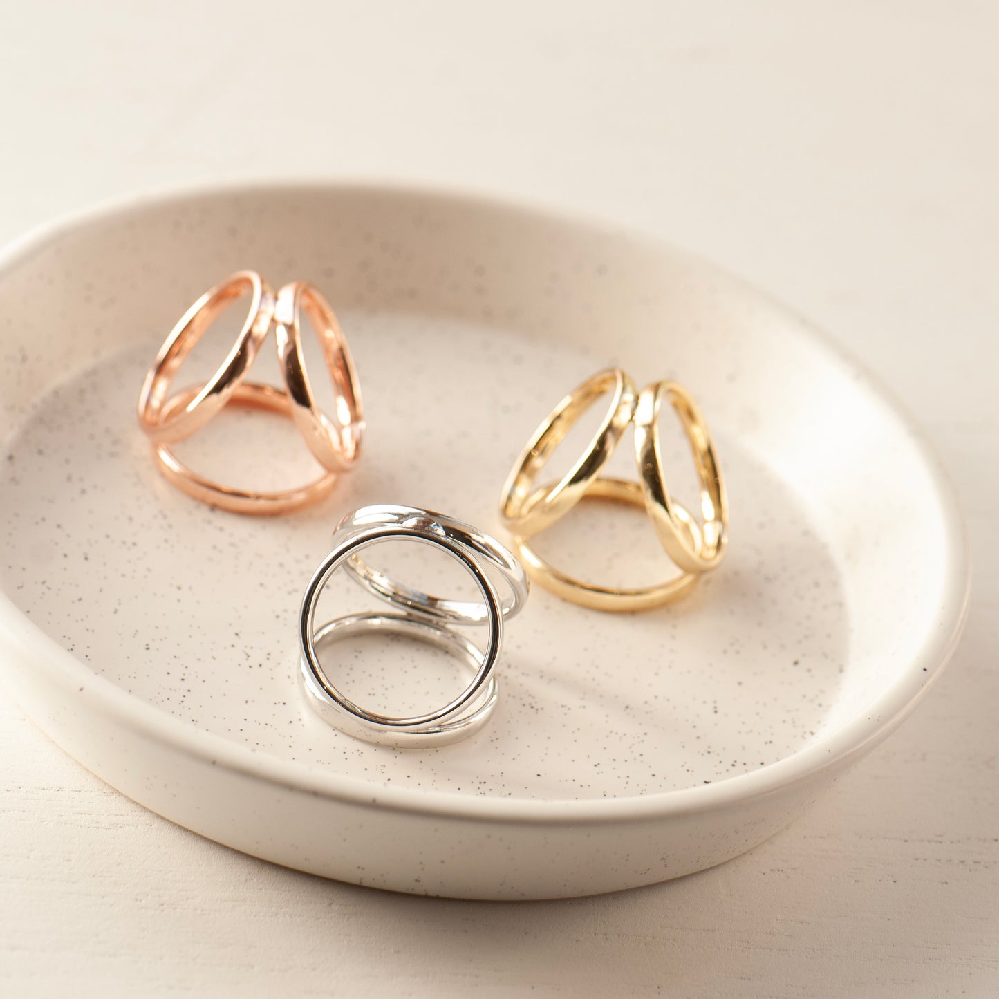 Three scarf rings in rose gold, gold, and silver on a white ceramic dish.