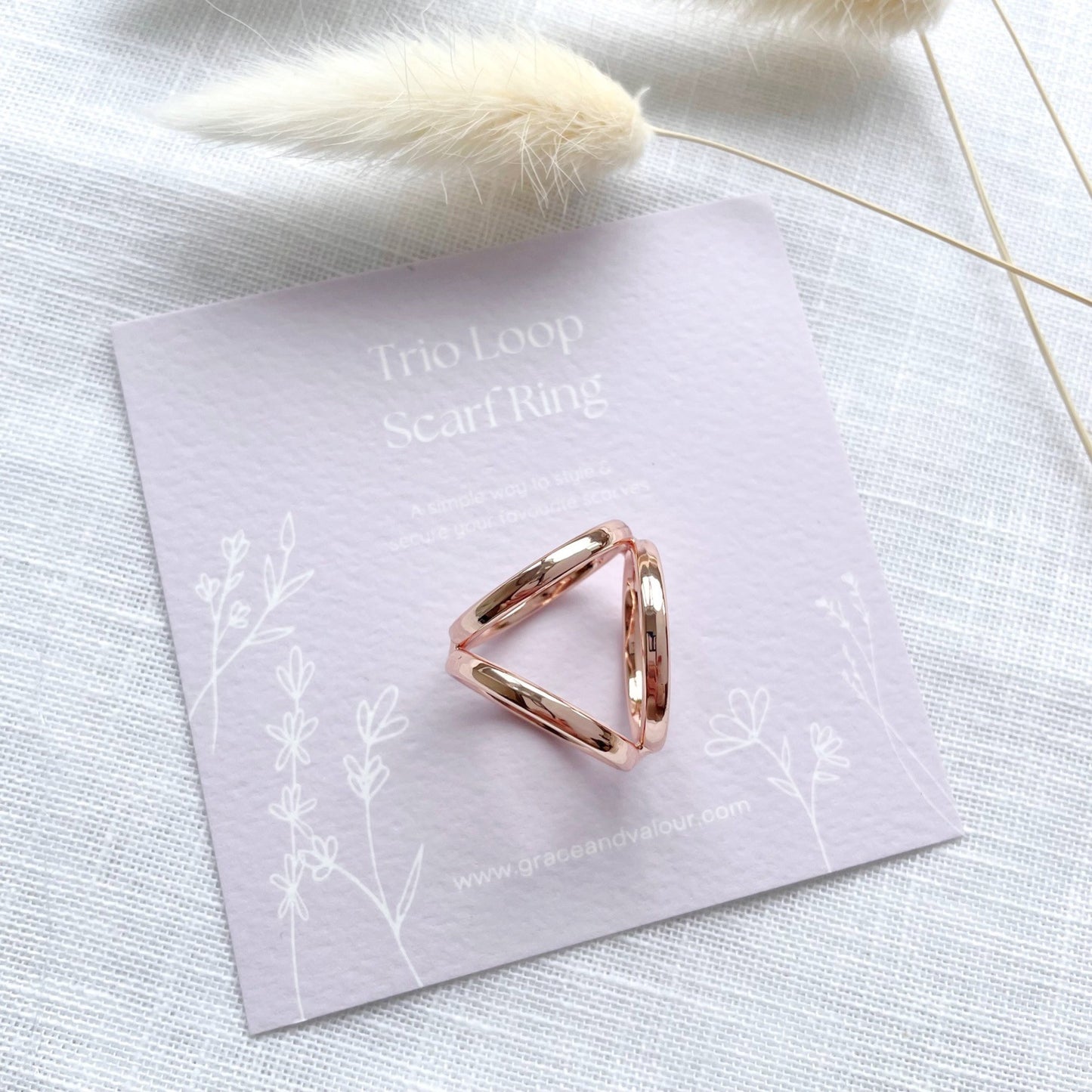 Rose gold scarf ring on a light purple card with floral designs, placed on a textured white surface.