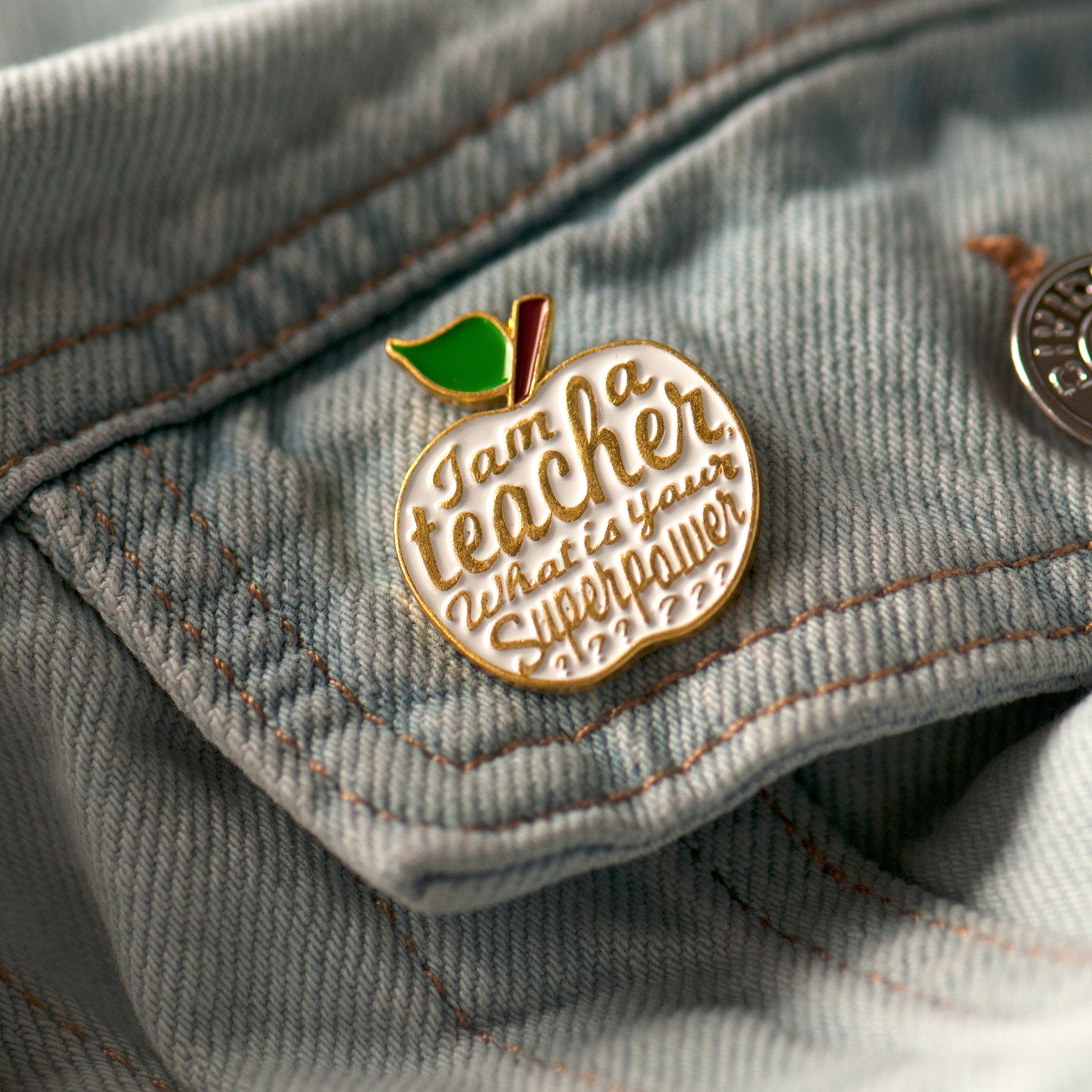 Pin on a denim jacket with an apple design and text 'I am a teacher, what is your superpower'.