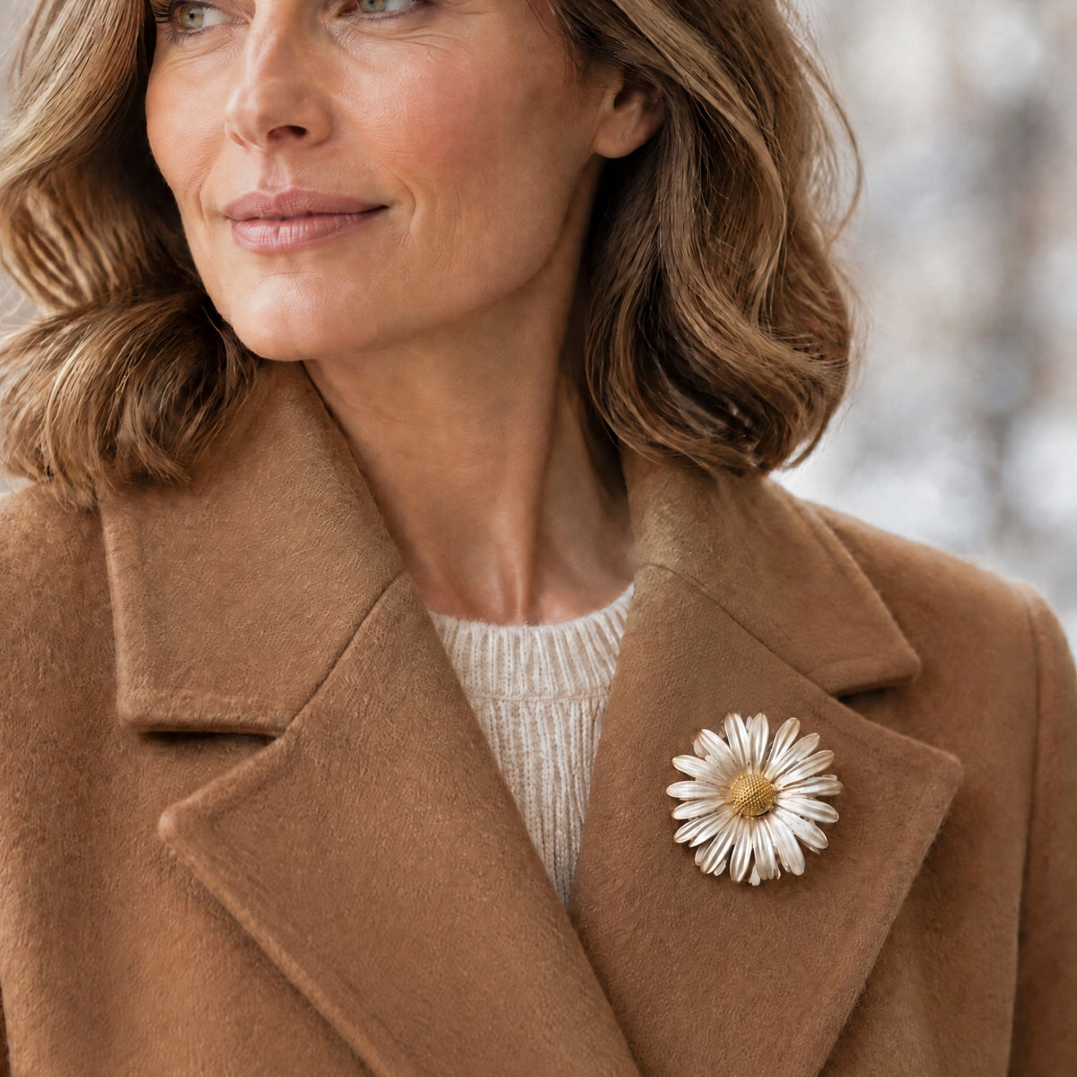 statement daisy gold and silver coloured brooch on the lapel of a camel coloured winter coat
